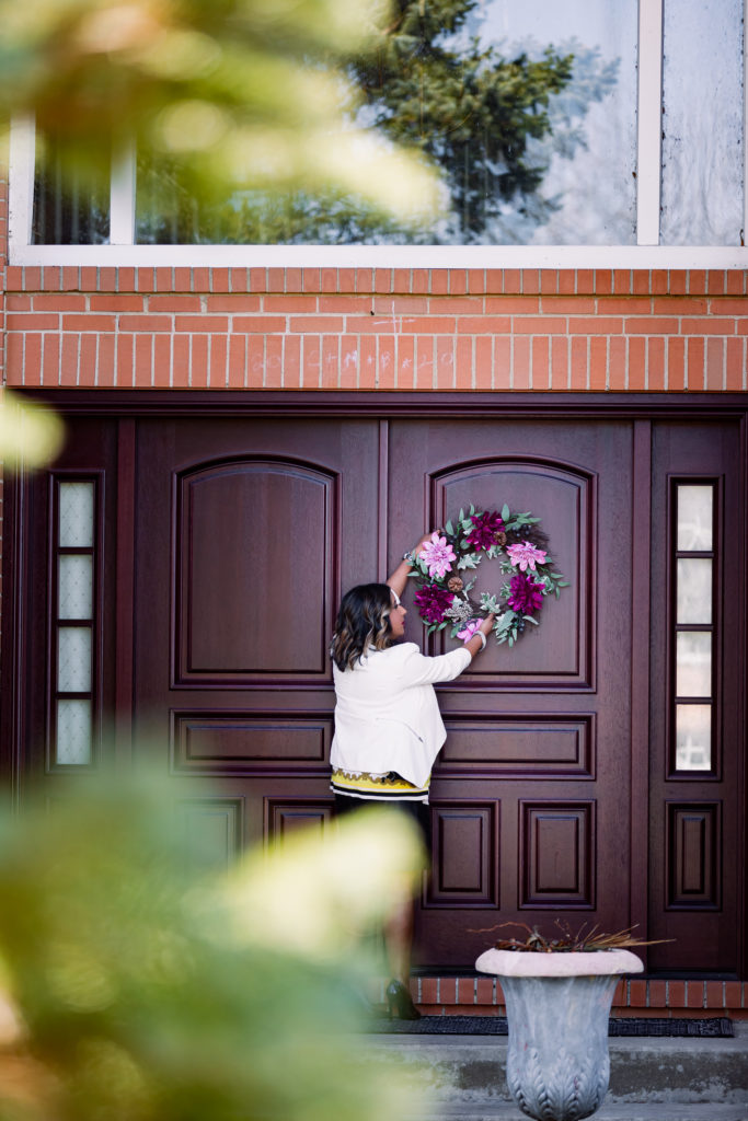 Woman Decorating Door to Big House with Flower Wreath