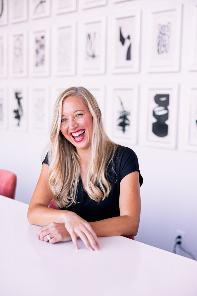 a blonde woman with red lipstick laughing in a business meeting room
