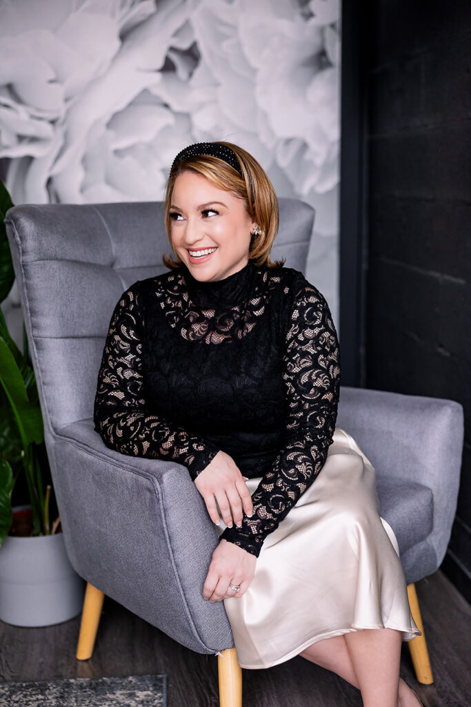 Vibrant and fun brand photo of a woman wearing a black lace blouse and satin skirt, sitting in a velvet chair, taken by This Way to Fabulous