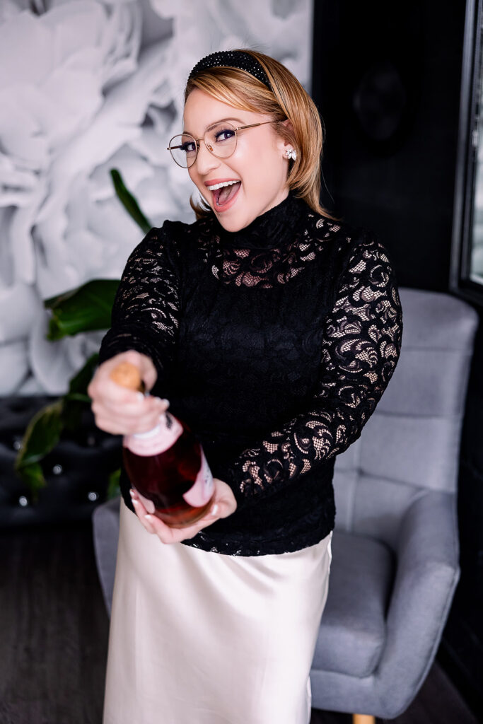 Vibrant brand photo of a woman in a black lace blouse and satin skirt holding a bottle of champagne, taken by This Way to Fabulous