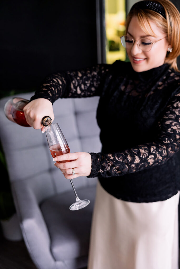 Vibrant brand photo of a woman in a black lace blouse and satin skirt pouring a bottle of champagne, taken by This Way to Fabulous