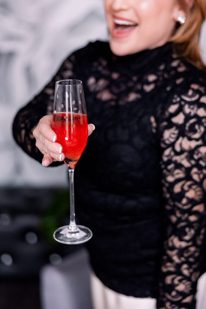 Vibrant brand photo of a woman in a black lace blouse and satin skirt holding a glass of champagne, taken by This Way to Fabulous