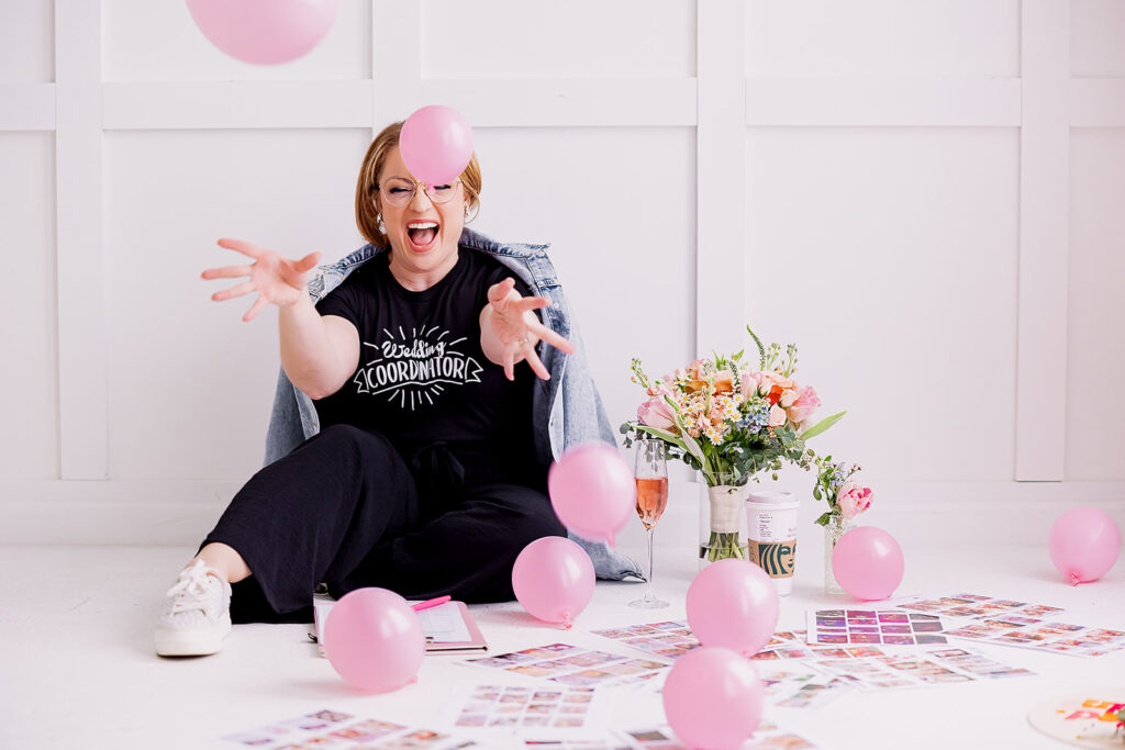 Vibrant and fun brand photo of a woman throwing pink balloons surrounded by flowers and mood boards, taken by This Way to Fabulous