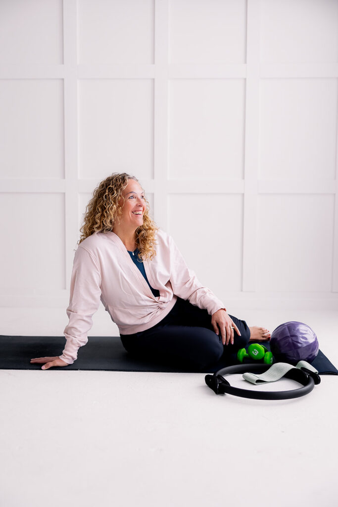 pilates instructor sitting on mat with equipment