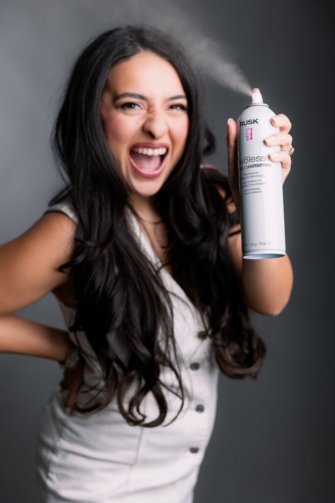 hair stylist spraying hairspray and smiling