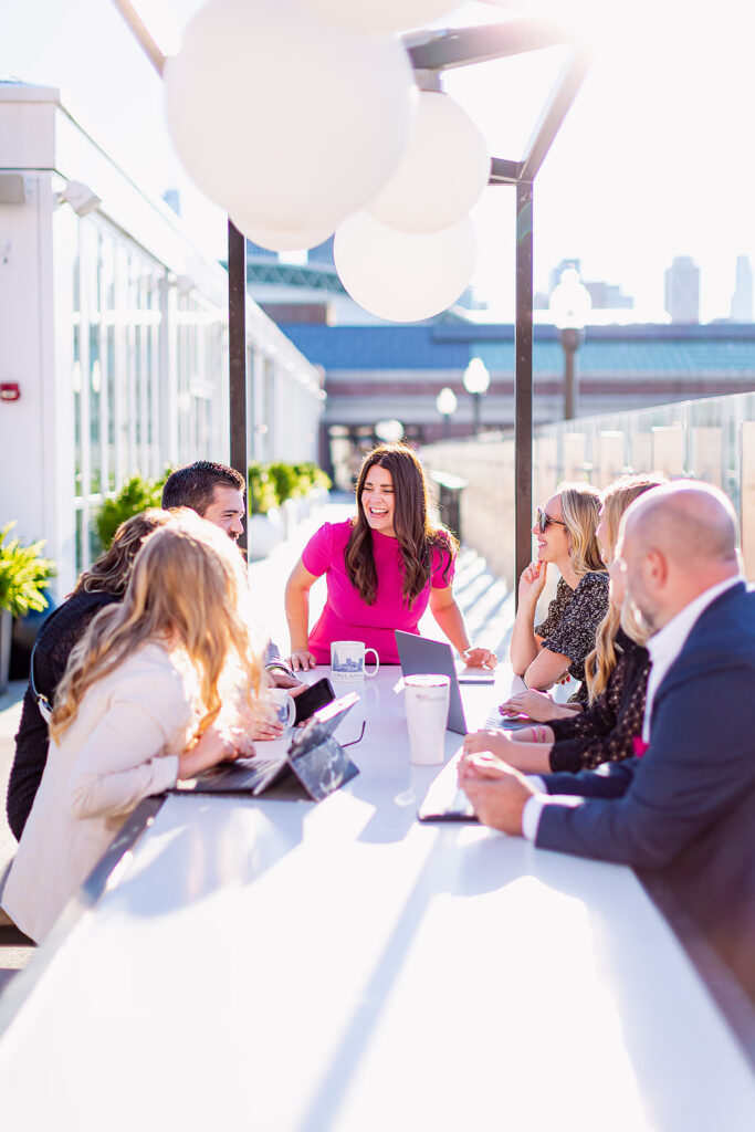 a professional team led by a woman in a pink shirt at the head of the conference table