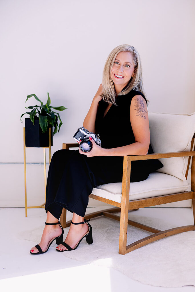 Lisa Kay of Lisa Kay Photography branding photo holding a camera sitting in a white chair