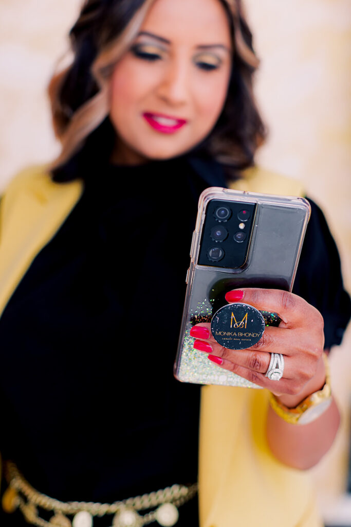 Luxury real estate agent Monika Bhondy holding a cell phone with a branded pop socket on the back
