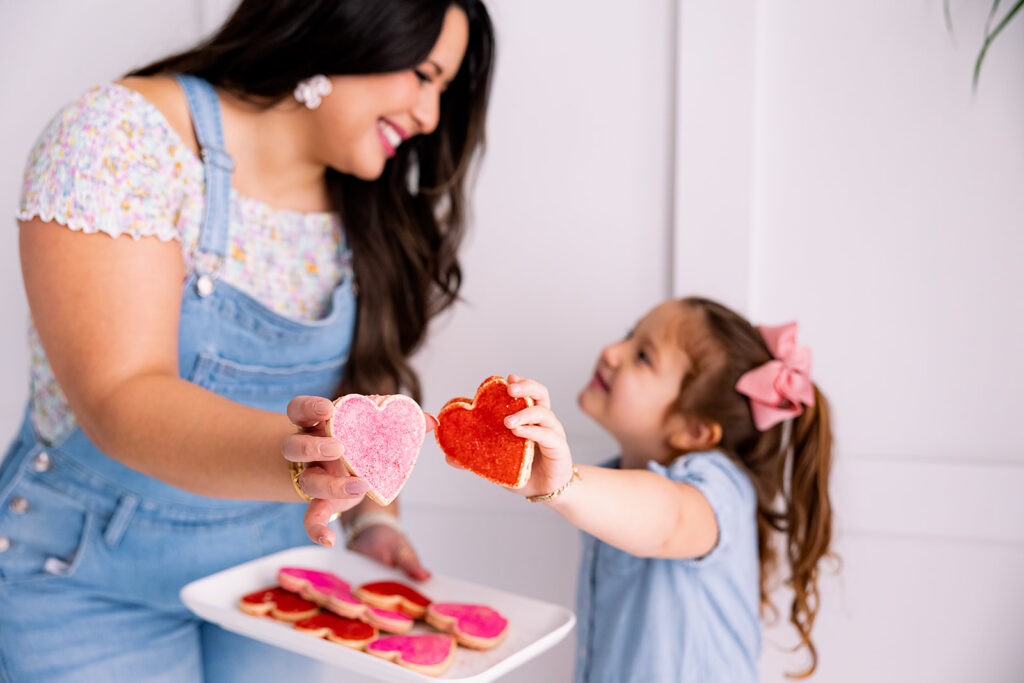 personal branding photo of Jacquelin Castillo of Mom Like a Boss wearing overalls holding heart cookies with her daughter photographed by This Way to Fabulous
