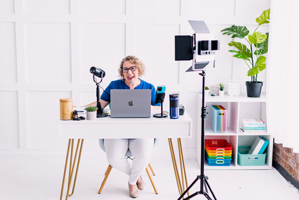 Amy from Clutter Care smiling in front of brightly colored office supplies and talking into her laptop during her professional organizer branding photoshoot by This Way to Fabulous