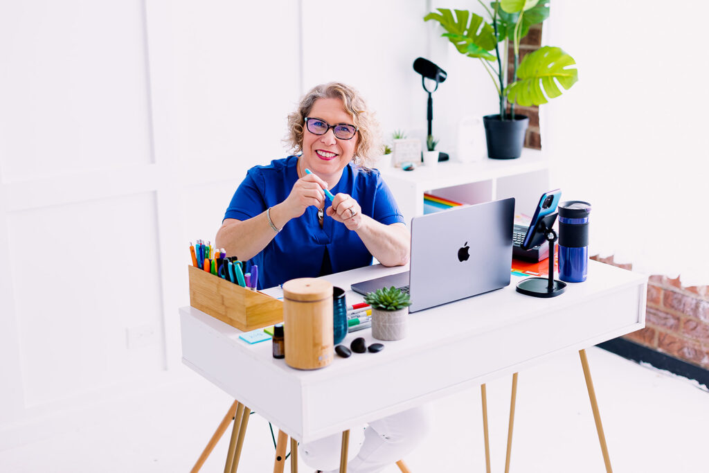 Amy from Clutter Care sitting in front of brightly colored office supplies during her professional organizer branding photoshoot by This Way to Fabulous
